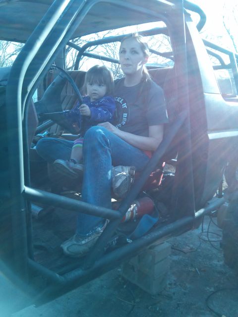 1986 Ford Bronco - A woman and child sit inside a heavily modified vehicle, suggesting off-road use.