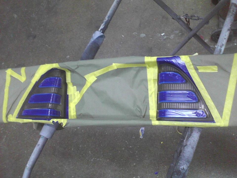 Two car taillights masked with tape and covered with a tarp, ready for painting