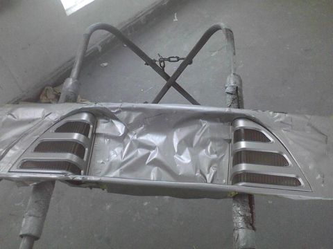 2003 Ford Crown Victoria - A car taillight assembly is prepared for painting, covered in masking tape and supported by a metal stand.