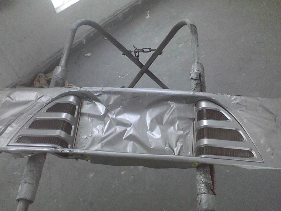 Car taillight assembly covered in silver masking tape, held by a stand