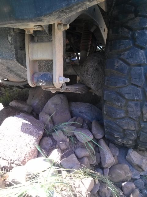 1981 Ford F-150 - Close-up view of the rear suspension and tire of a vehicle, situated amongst rocks and grass.