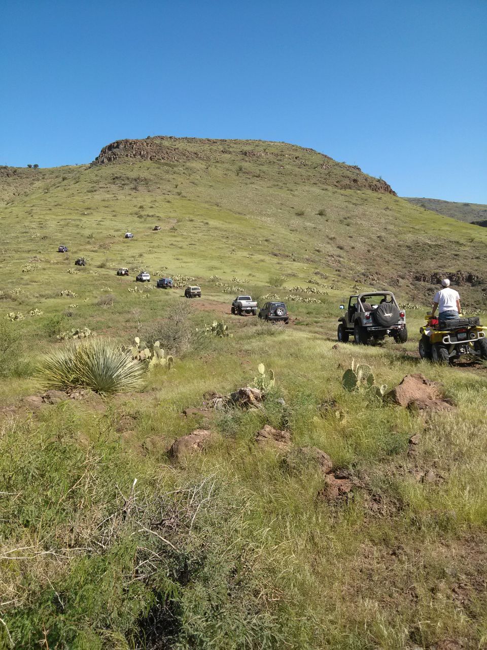 Off-road vehicles driving on a grassy hill under a clear blue sky