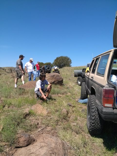 1981 Ford F-150 - Several people gather around off-road vehicles on a sunny day in a grassy, rocky landscape.