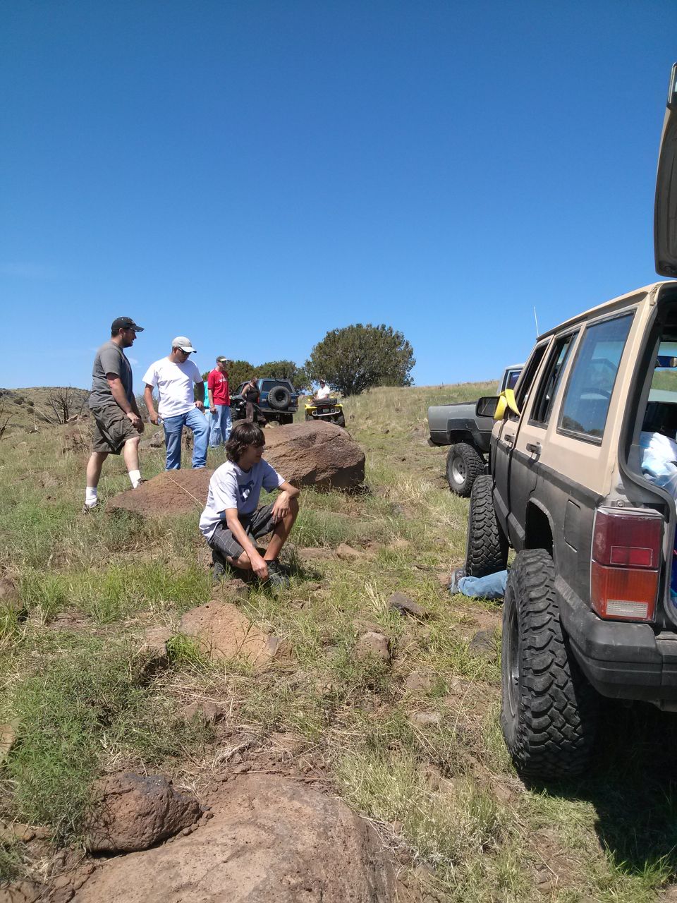 Tan Jeep Cherokee XJ parked on grassy hill with people around