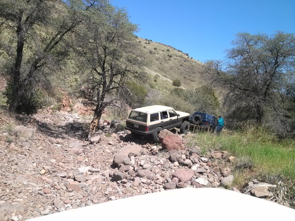 Two Jeep Cherokee XJs on a rocky, off-road trail. One is tan and brown, the other is dark blue