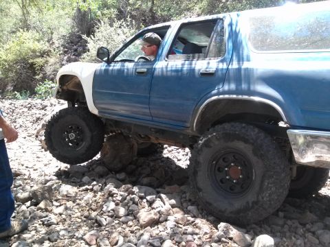 1981 Ford F-150 - A blue SUV with prominent white fender flares is shown traversing a rocky, off-road path.