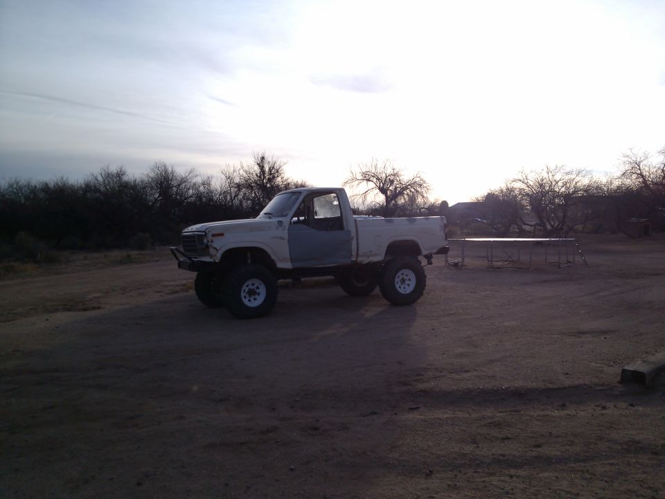 White pickup truck with large tires and mismatched doors, parked outdoors