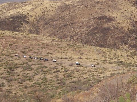 1981 Ford F-150 - A group of off-road vehicles travels along a dusty track in a barren, mountainous region.