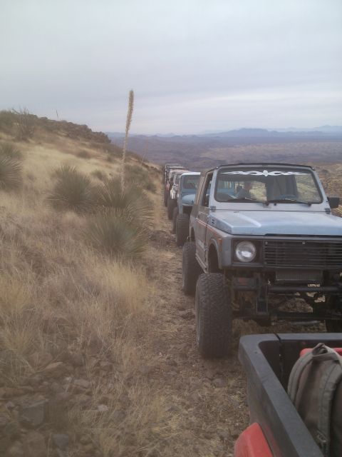 1981 Ford F-150 - A convoy of off-road vehicles navigates a dry, mountainous terrain under an overcast sky.