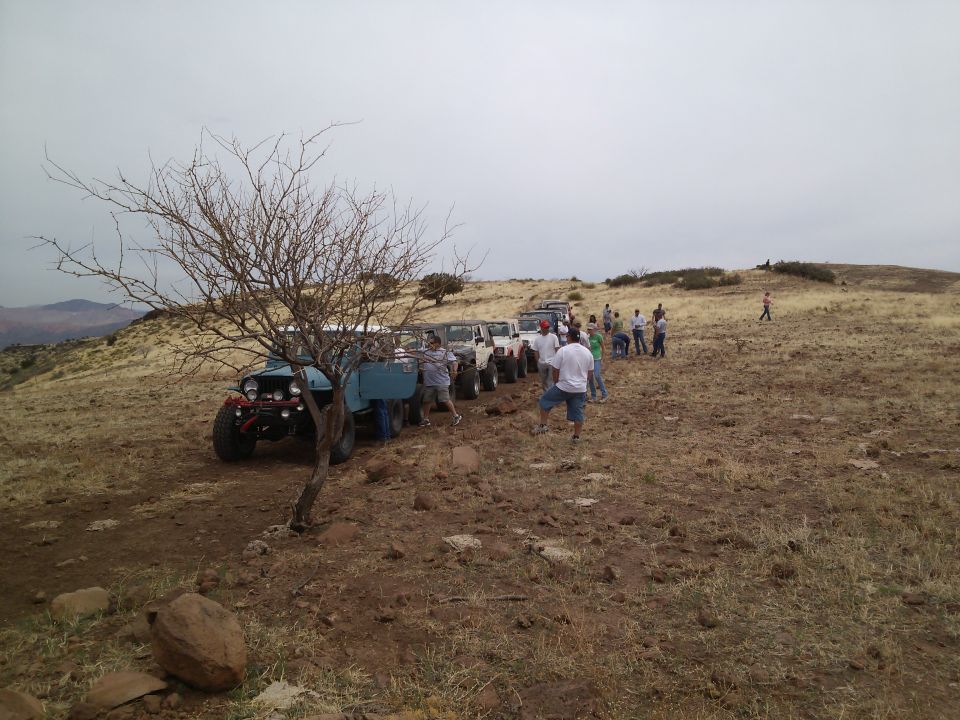 Several off-road vehicles lined up on a muddy trail with people standing around them