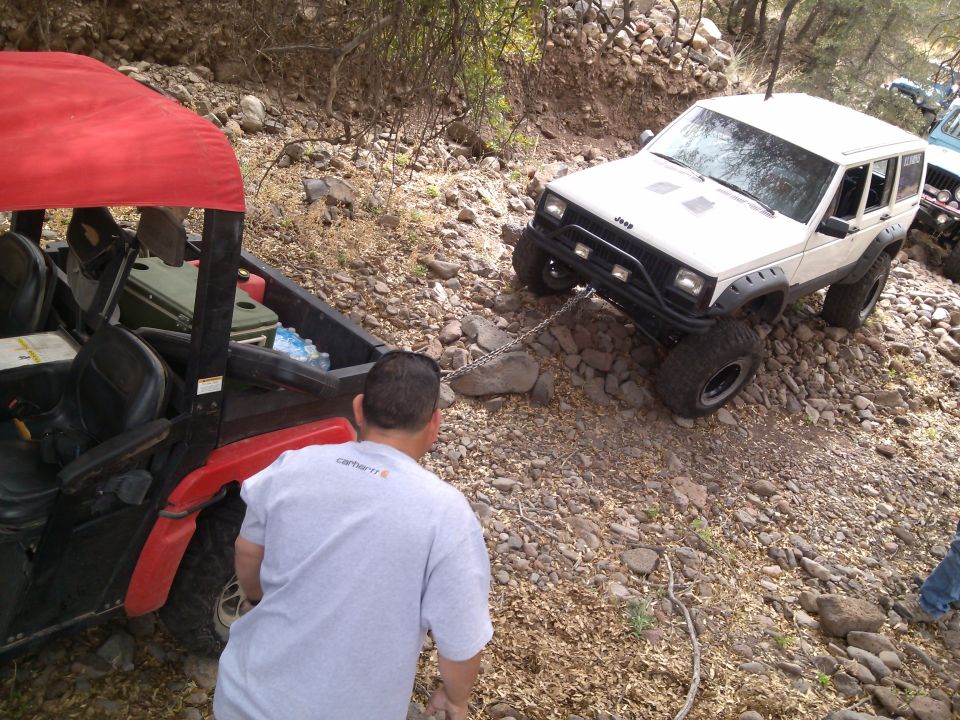 White Jeep Cherokee being towed by a red UTV on a rocky trail