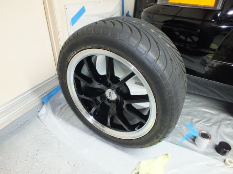 2003 Ford Crown Victoria - black polished-lip wheel with tire leaned against a taped garage wall during a brake job.