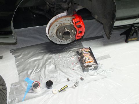 2003 Ford Crown Victoria - Freshly painted red caliper on a drilled-slotted rotor, with lug nuts and supplies on the floor.