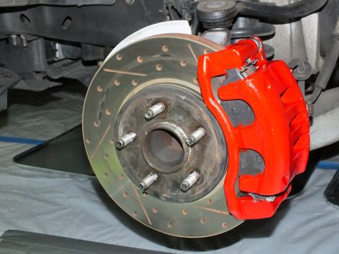 2003 Ford Crown Victoria - Detail of a red front caliper mounted to a drilled-slotted rotor on a five-lug wheel hub.