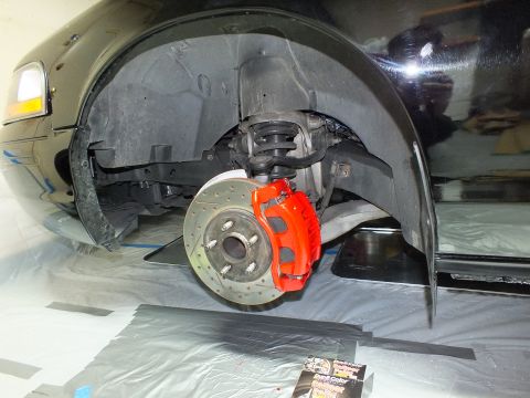 2003 Ford Crown Victoria - Red-painted caliper and cross-drilled rotor mounted at the front of a black vehicle raised on jack stands.