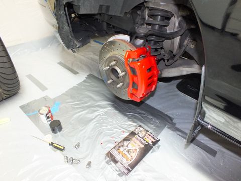 2003 Ford Crown Victoria - Completed front brake assembly with red caliper, plus paint can, screwdriver and lug nuts laid out on the floor.