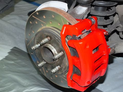2003 Ford Crown Victoria - Detail of a freshly painted red caliper clamped over a drilled and slotted rotor on a five-lug hub.