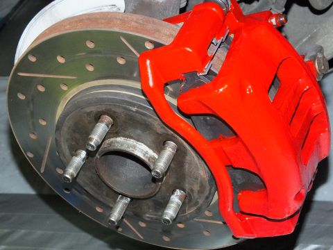 2003 Ford Crown Victoria - Side detail of a red caliper and cross-drilled rotor on a five-stud hub against a covered floor.