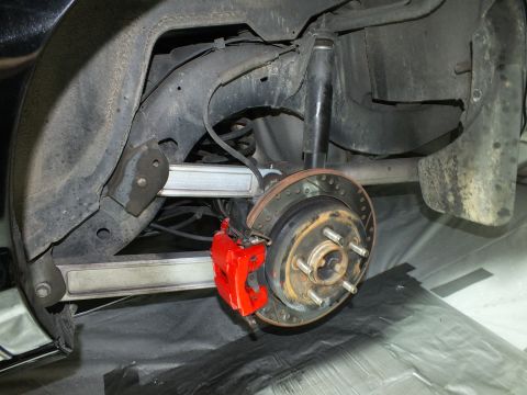 2003 Ford Crown Victoria - Rear brake setup with red caliper and drilled rotor exposed in the wheel well of a black vehicle.