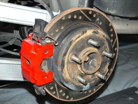 2003 Ford Crown Victoria - Rear red caliper clamped on a drilled rotor over a five-stud hub beside a silver control arm.