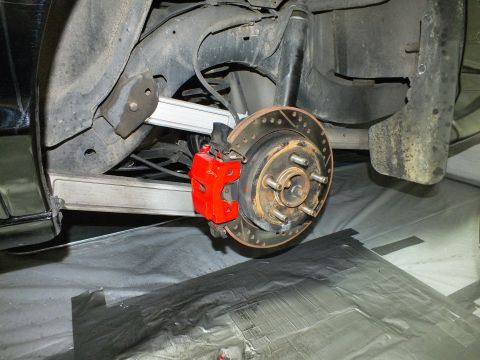 2003 Ford Crown Victoria - Installed rear brake with red caliper and drilled rotor in the wheel well of a black vehicle.