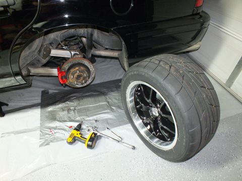2003 Ford Crown Victoria - Rear hub exposed on a black vehicle next to a removed black multi-spoke wheel with a wide street tire.