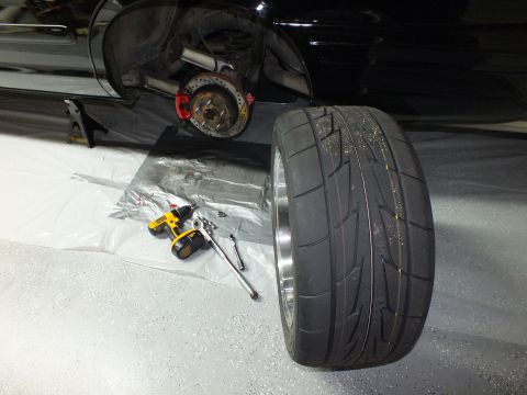 2003 Ford Crown Victoria - Wide-tire black wheel leaning beside a raised black vehicle with a cordless drill and tools on the floor.