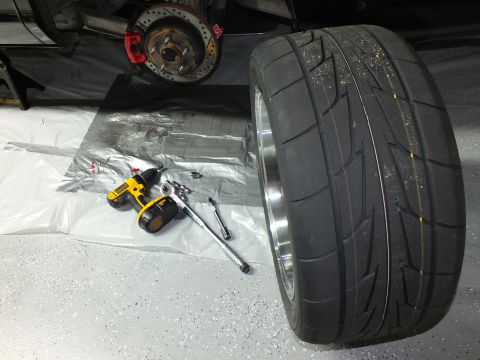 2003 Ford Crown Victoria - Polished-lip black wheel and performance tire beside an exposed hub, with a yellow cordless drill on the floor.