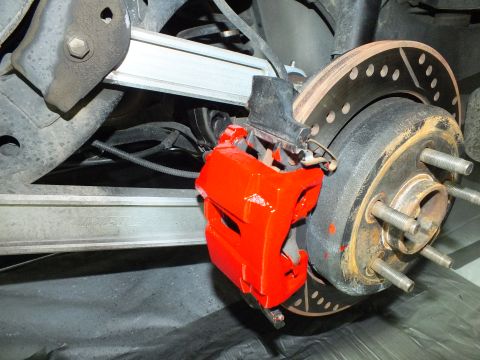 2003 Ford Crown Victoria - Rear red caliper and drilled rotor mounted near a polished aluminum trailing arm beneath the vehicle.