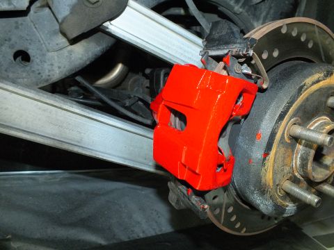 2003 Ford Crown Victoria - Close rear view of a red caliper on a drilled rotor next to a polished aluminum control arm.