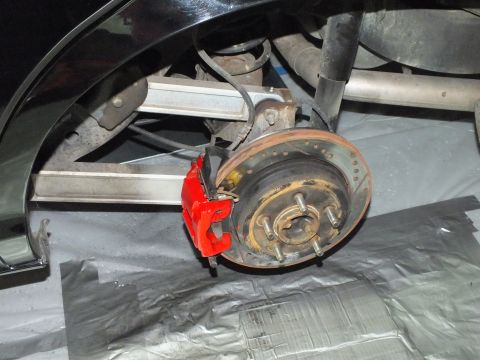 2003 Ford Crown Victoria - Rear hub with red caliper exposed beneath the fender of a black vehicle raised on jack stands.