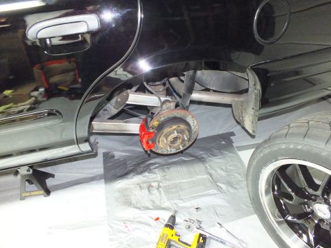 2003 Ford Crown Victoria - Side view of a black vehicle on jack stands, rear hub bare, with a removed wheel and tools on the floor.