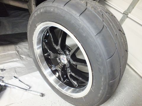 2003 Ford Crown Victoria - Black multi-spoke wheel with polished lip and a wide performance tire standing on a garage floor.