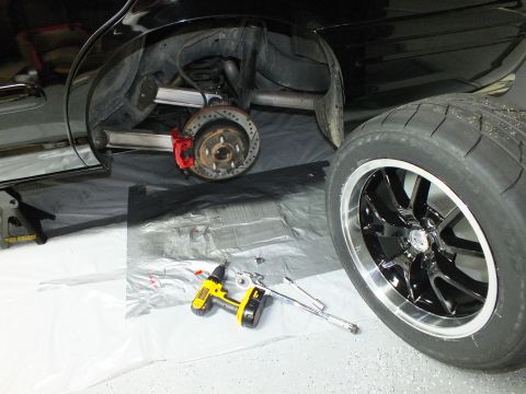 2003 Ford Crown Victoria - Rear of a black vehicle on jack stands with exposed hub, a black wheel and a yellow drill on the floor.