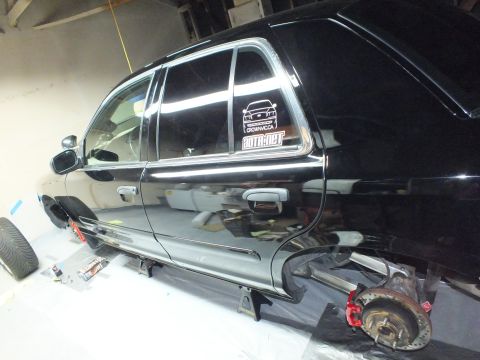 2003 Ford Crown Victoria - Side profile of a black SUV on jack stands showing a supermotors.net rear-window decal and exposed front hub.