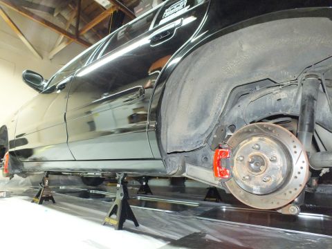 2003 Ford Crown Victoria - Underside view of a lowered black sedan supported on jack stands, exposing a drilled front rotor and red brake caliper.