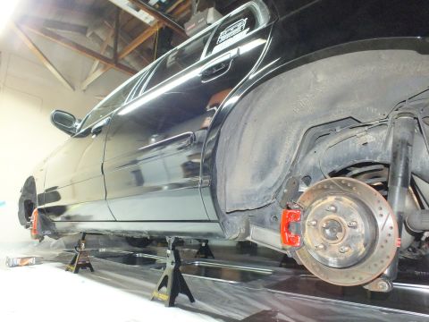 2003 Ford Crown Victoria - Rocker and front wheel area of a black sedan on jack stands, drilled brake rotor and red caliper exposed.