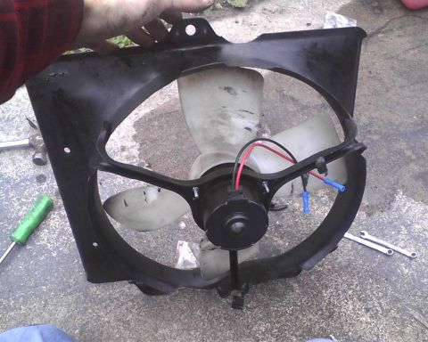 1991 Toyota Celica - A radiator fan assembly is held by a hand, with tools nearby on the ground.