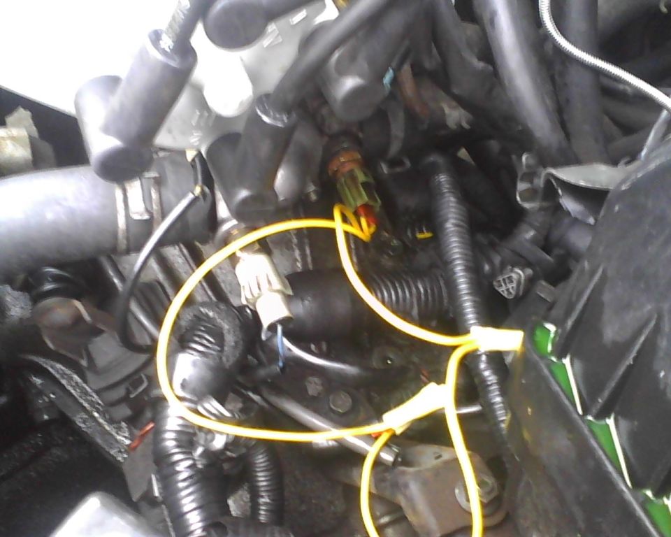 Engine bay with yellow wires connected to sensors and various hoses and conduits