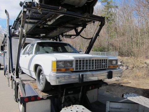 1991 Ford LTD Crown Victoria - A white sedan, likely a 1988 model, is loaded onto a car carrier.