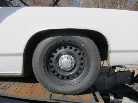 1991 Ford LTD Crown Victoria - White car's front wheel and fender detail, showing a black steel wheel with a silver hubcap.