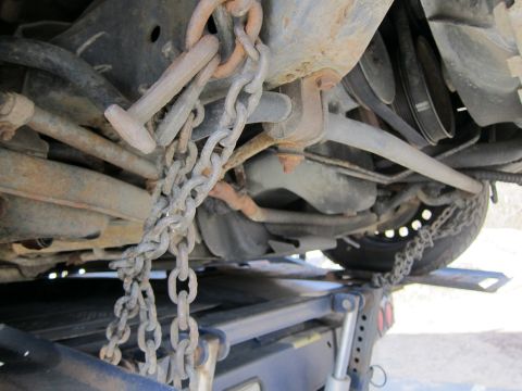 1991 Ford LTD Crown Victoria - The underside of a vehicle is secured with chains to a tow truck bed.