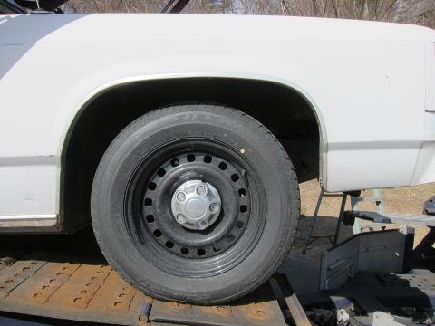1991 Ford LTD Crown Victoria - Close-up of a white car's fender and wheel, resting on a trailer.