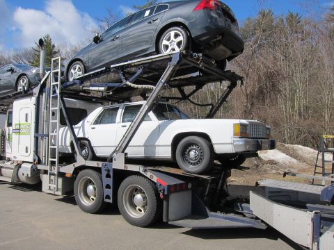 1991 Ford LTD Crown Victoria - A white sedan is transported on a car carrier, with another vehicle on the upper deck. The truck has 'WE MOVE CARS' branding.