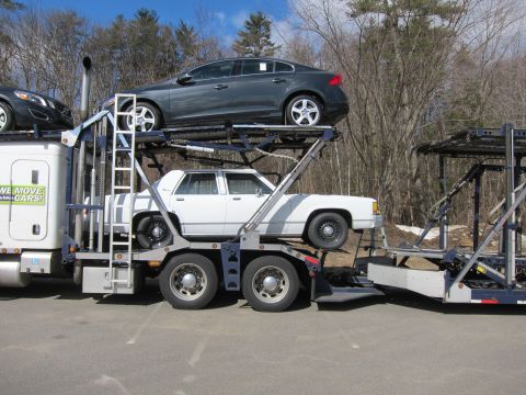 1991 Ford LTD Crown Victoria - Car carrier truck transporting a white sedan and a dark sedan. The white sedan appears to be a 1991 Ford Crown Victoria LTD.