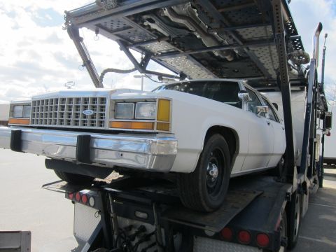 1991 Ford LTD Crown Victoria - White Ford Crown Victoria on a car carrier, front quarter view, showing its chrome grille and bumper.