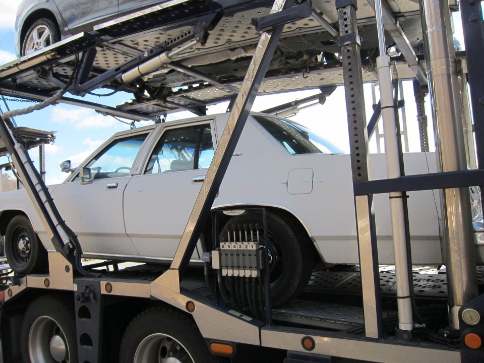 White sedan on a car carrier, another car above it