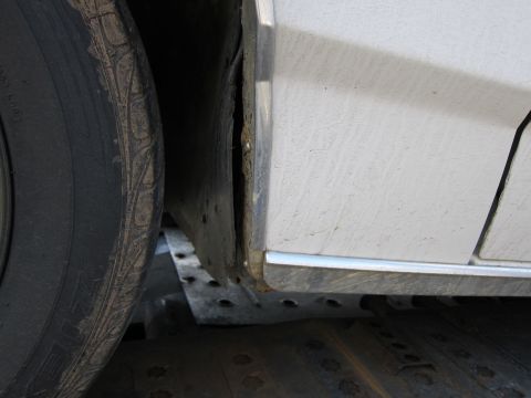 1991 Ford LTD Crown Victoria - Close-up of a white car's side, showing the wheel well and lower body panel with visible dirt and chrome trim.