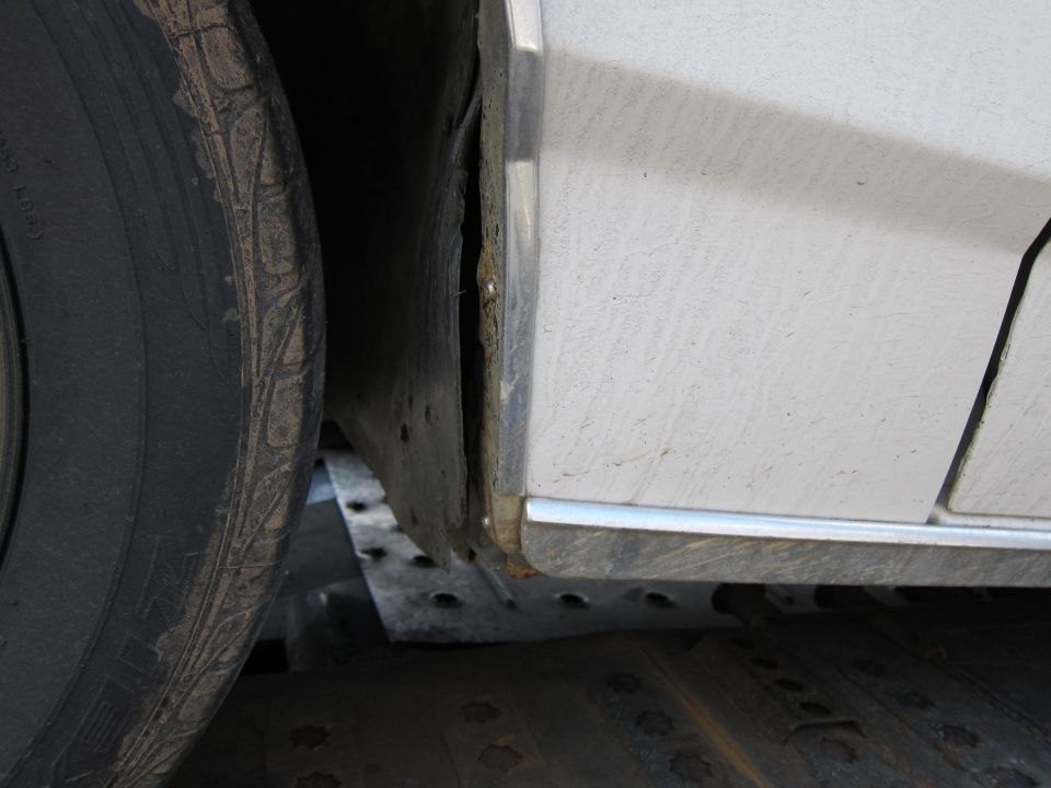 White car's dirty wheel well and lower body panel with chrome trim