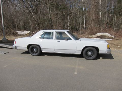 1991 Ford LTD Crown Victoria - A white sedan with a boxy body style is parked outdoors on a paved surface.
